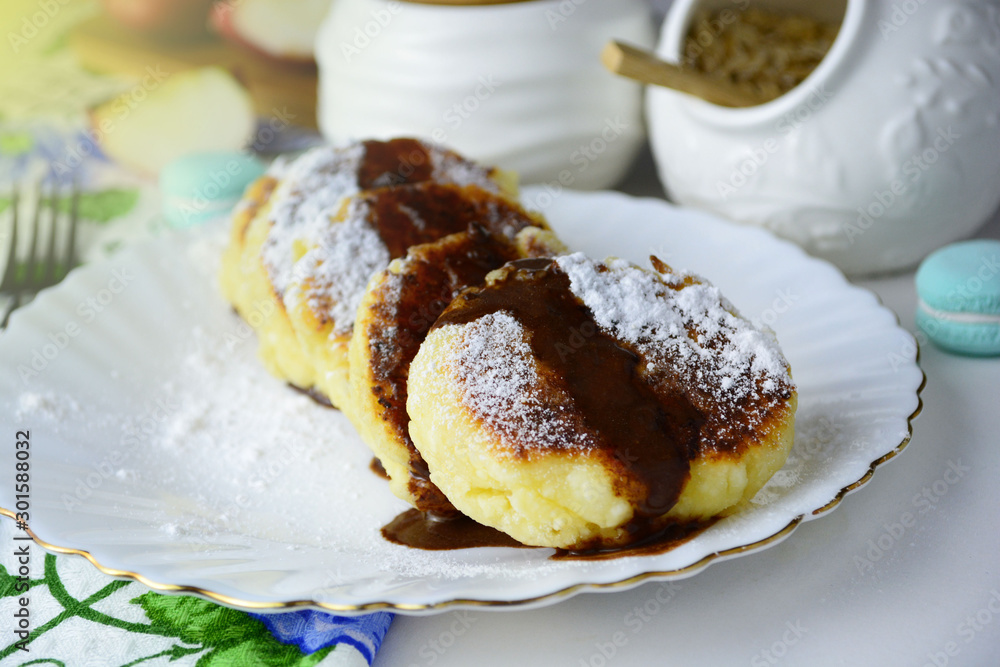 Curd fritters, syrniki. On a plate syrniki with chocolate. Next a bowl of sugar. Curd fritters, syrniki. On a plate syrniki with chocolate. Next a bowl of sugar.