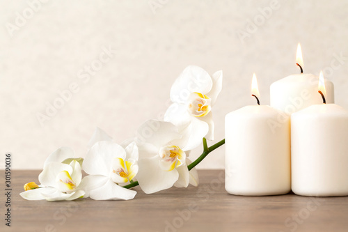 Spa still life with flowers orchids and burning aromatic candles. Copy space. White flowers of Orchid with candles on wooden table. 