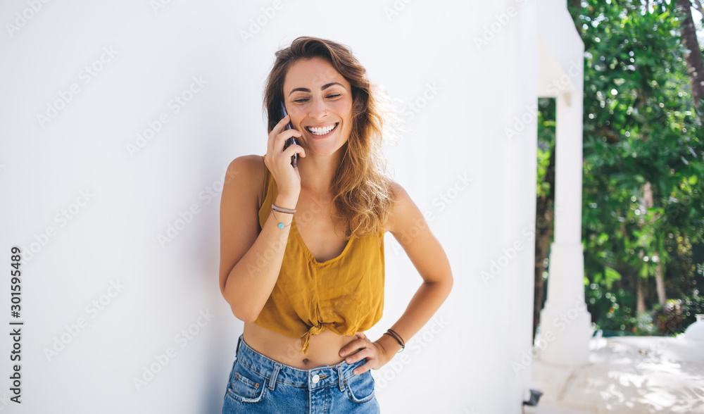 Fototapeta premium Cheerful modern fit young woman in casual outfit having phone call while standing on gray background