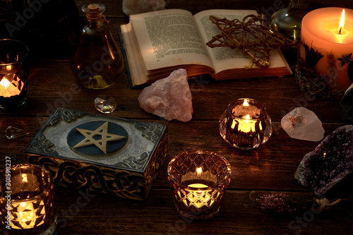 Esoteric or mystical still life with a box and a few burning candles, a pentagram next to an open book. Pendulum and precious stones