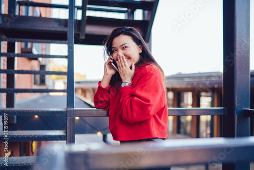 Cheerful female teenager enjoying friendly smartphone conversation for intriguer gossiping and rumors, happy chinese hipster girl making international smartphone conversation connected to roaming photo