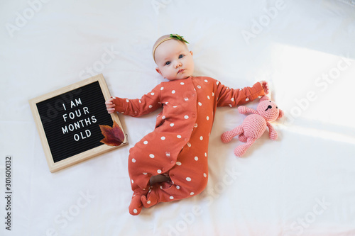 Four months old baby girl laying down on white background with letter board and teddy bear. Flat lay composition. photo