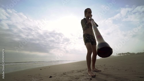 Young musician man playing on didgeridoo on beach at sunset.
