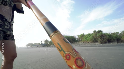 Young musician man playing on didgeridoo on beach at sunset. photo