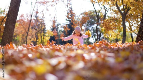 Little kid girl in a pink coat playing in autumn park with chestnut lift it up from a dry grass
