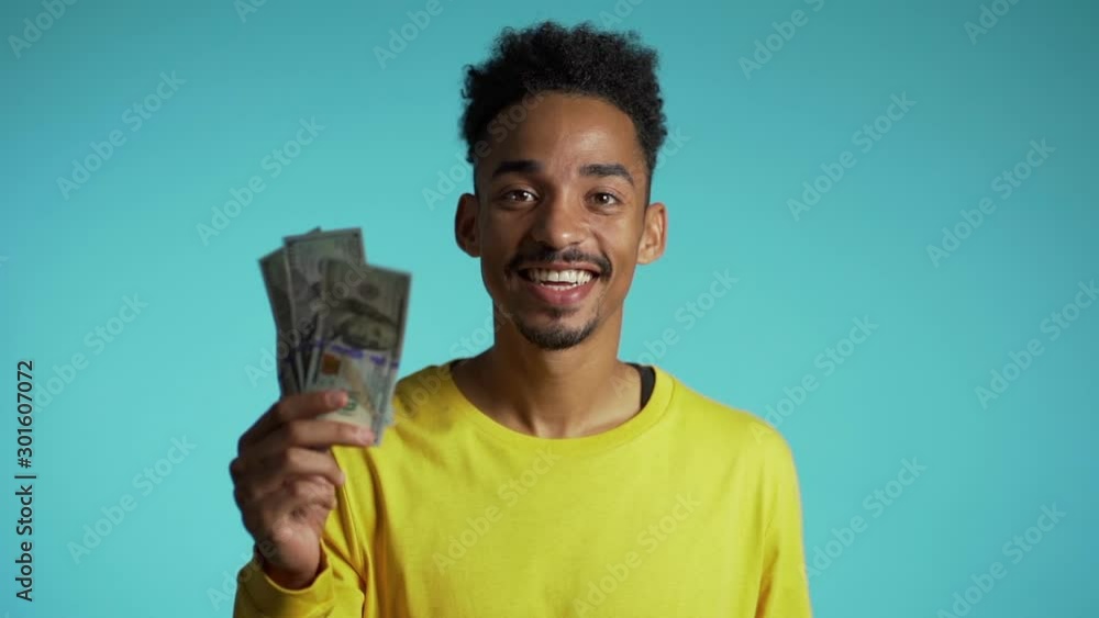 Satisfied african man showing money - U.S. currency dollars banknotes on blue wall. Symbol of success, gain, victory. Slow motion Satisfied african man showing money - U.S. currency dollars banknotes on blue wall. Symbol of success, gain, victory. Slow motion