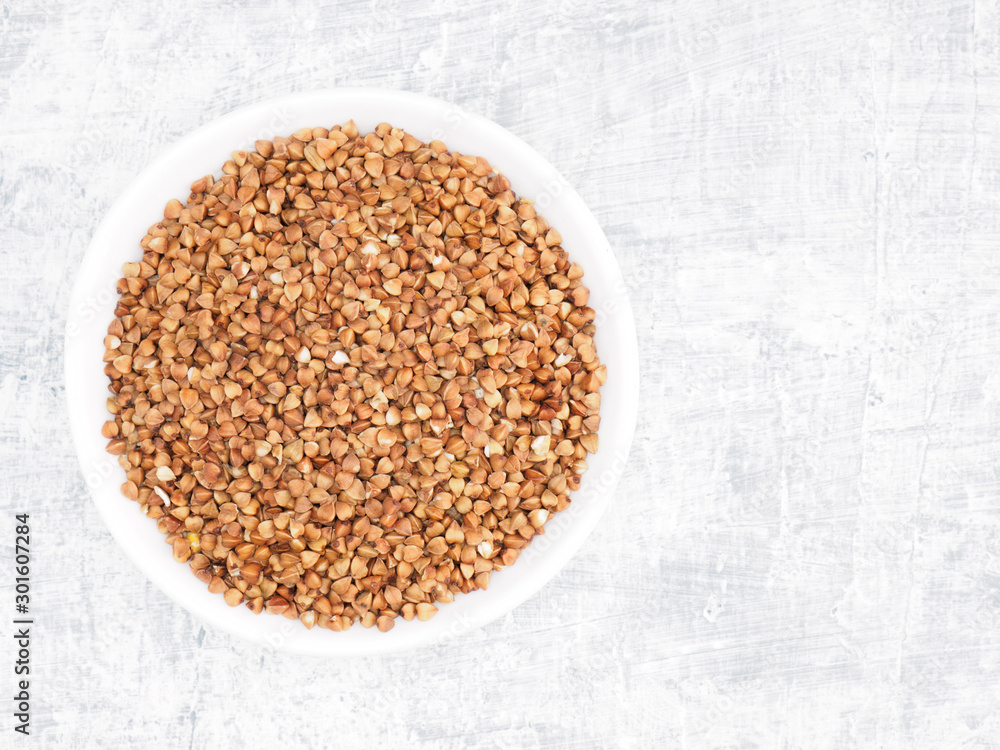 Buckwheat groats in a ceramic bowl on a white cement background. Healthy eating concept Buckwheat groats in a ceramic bowl on a white cement background. Healthy eating concept