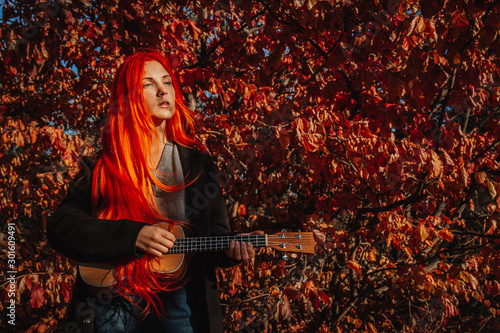 Sexy redhead girl with long hair plays the ukulele. Perfect woman portrait. Gorgeous strong and thick hair. Deep blue eyes. Natural beauty  clean skin  face and hair care.
