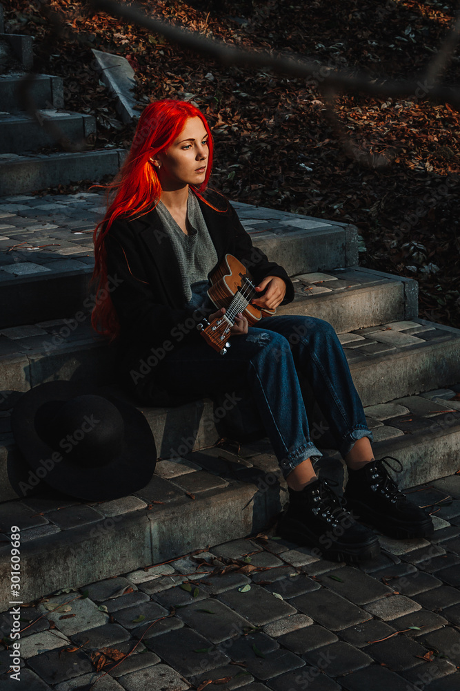 Fototapeta premium Sexy redhead girl with long hair plays the ukulele. Perfect woman portrait. Gorgeous strong and thick hair. Deep blue eyes. Natural beauty, clean skin, face and hair care.