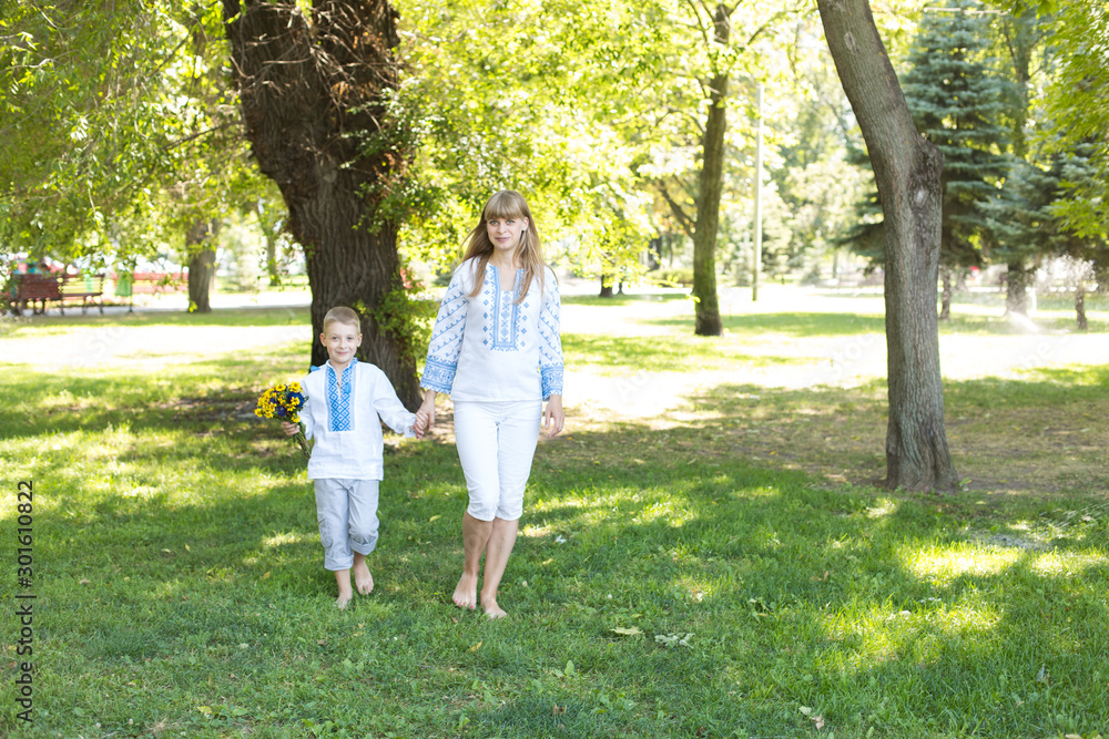 mother and son in embroidered shirts walk barefoot on the grass. national clothes of Ukraine. mother and son in embroidered shirts walk barefoot on the grass. national clothes of Ukraine.