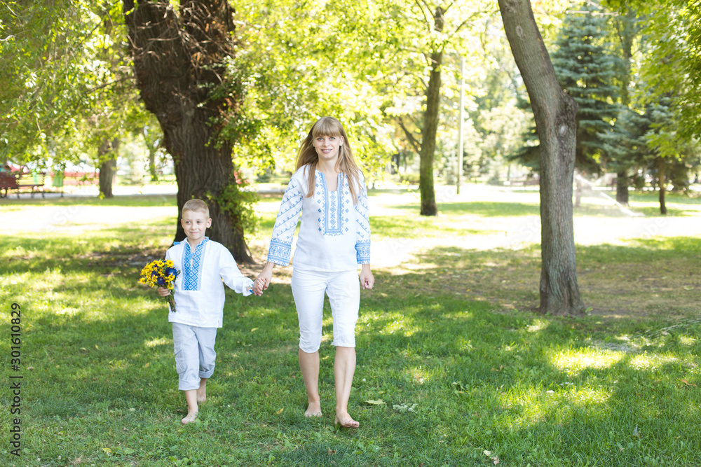 mother and son in embroidered shirts walk barefoot on the grass. national clothes of Ukraine.
