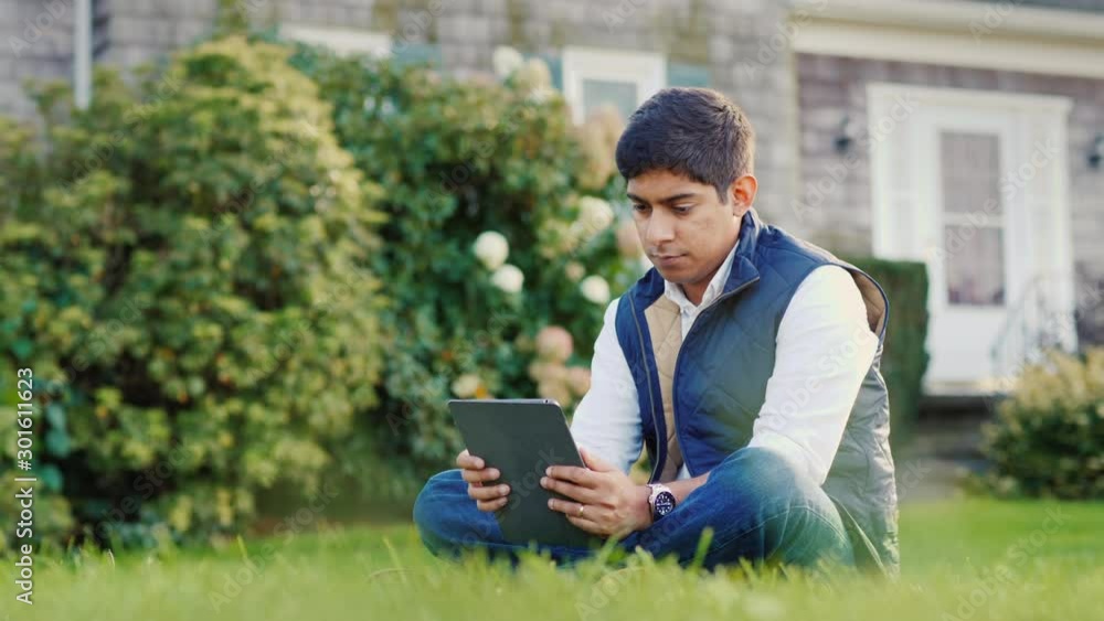 Indian man uses a tablet in the backyard of his house Indian man uses a tablet in the backyard of his house