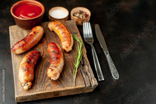 Grilled sausages with spices, ketchup and rosemary on a stone table, ready to eat