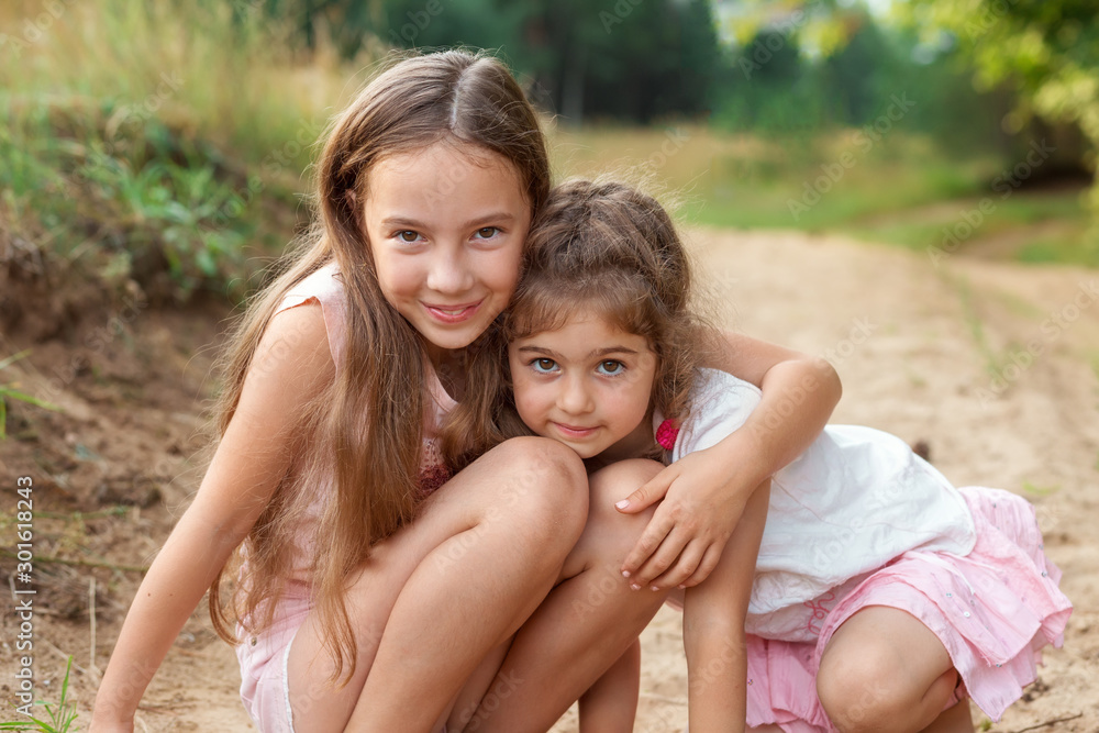 Portrait of Two Cute little girls embracing and laughing at the forest. Happy kids outdoors Portrait of Two Cute little girls embracing and laughing at the forest. Happy kids outdoors