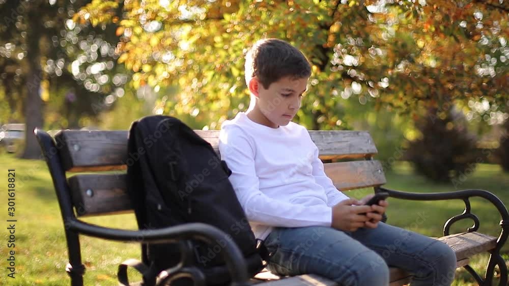 Schoolboy use phone in the park after lesson. Teenage boy use smartphone outside. Gold autumn Schoolboy use phone in the park after lesson. Teenage boy use smartphone outside. Gold autumn