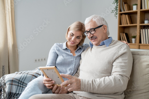 Senior man in casualwear showing his happy young daughter photo in frame