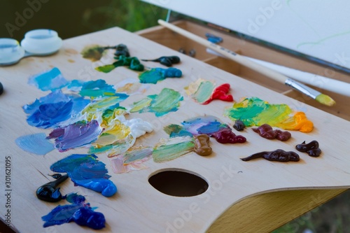 painter wooden palette with a mix of fresh bright colorful oil paints in disorder, clean brushes rest at a break during summer plainair painting, artist creative inspiration in soft pastel light photo