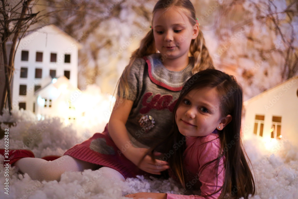 Obraz premium two girls in Christmas decorations with artificial snow and small cardboard houses