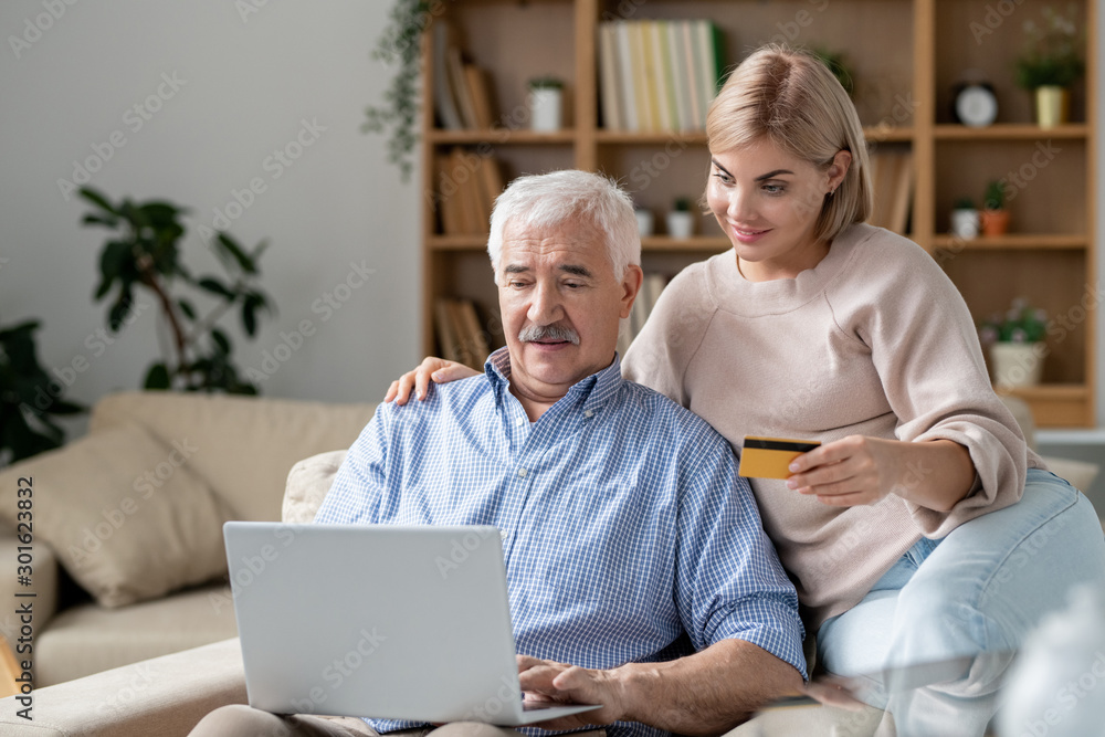 Pretty young woman with credit card sitting by her senior father shopping online