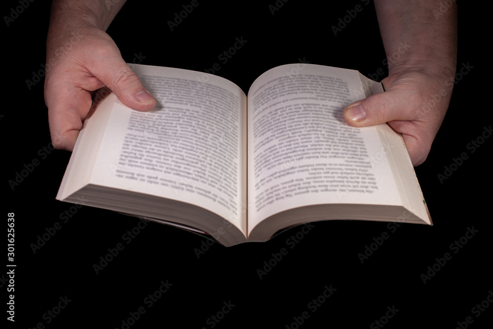 Fototapeta premium Ein aufgeschlagenes Buch von zwei Händen gehalten vor schwarzem Hintergrund
