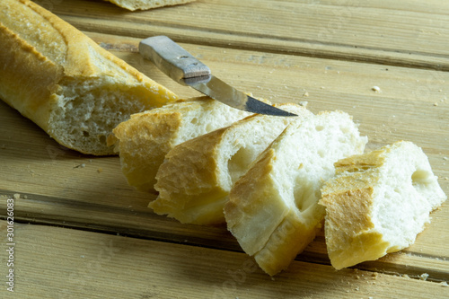 Freshly baked traditional french bread on a wooden table next to a kitchen knife. Sliced french baguette.
