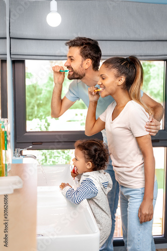 Husband, wife and kid girl brushing teeth in bathroom