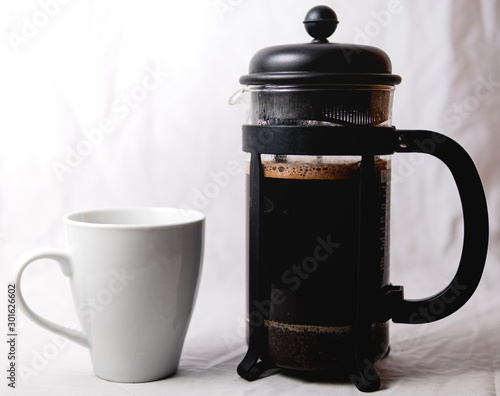 A french press and a cup of coffee sitting next to each other