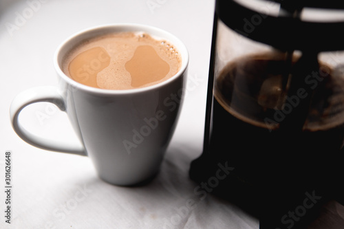 A full cup of coffee sitting next to a french press