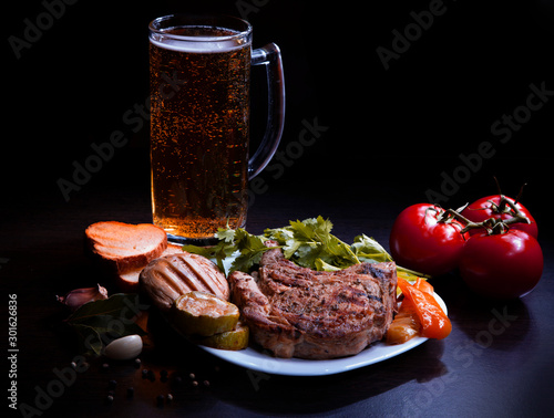 grilled meat and vegetables on a plate with fresh tomatoes and beer