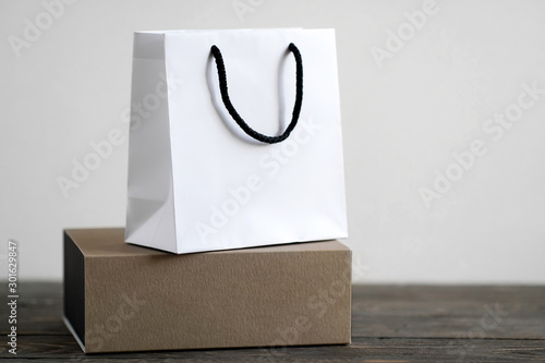 White paper bag and craft gift box on wooden table. Brand packaging concept. Copy space for text