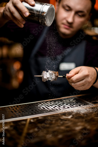 Professional bartender adding a sugar powder to the brownie pieces on the skewer