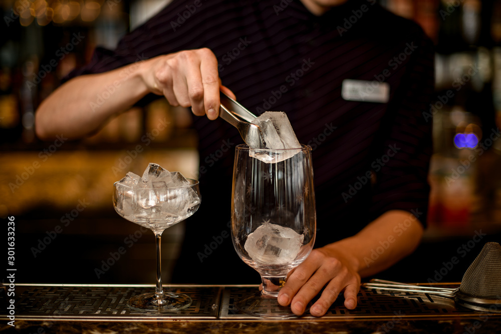 Male bartender putting an ice cube with tweezers to the empty cocktail  glass Stock Photo | Adobe Stock