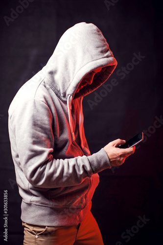 Man wearing hoody sweater with phone in hands. Crime and hacking concept