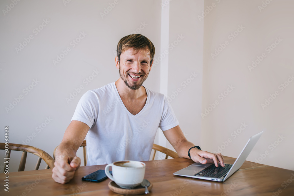 Optimistic male resting at table and working on laptop Optimistic male resting at table and working on laptop