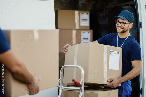 Happy manual worker unloading cardboard boxes from delivery van. photo