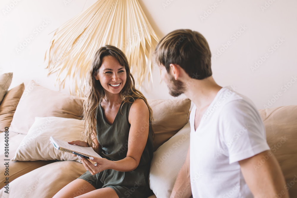 Obraz premium Cheerful man and woman discussing funny information or publication from social network during leisure day in home interior, positive hipster guys enjoying fellow relationship in cozy apartment