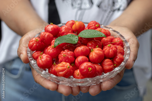 Ebony woman serving a glass plate full of fresh pitanga fruits