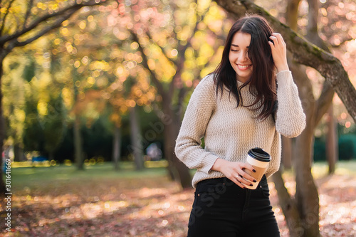 Beautiful woman drink coffee and posing for the camera in autumn park.
