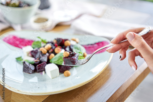 Woman eats Italian salad with beetroot, basil leaves and cheese feta, with oil and small profiteroles. Healthy diet food.