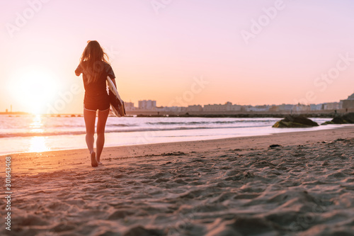 against the background of a beautiful sunset, the girl goes into the distance along the ocean in her hand surfboard