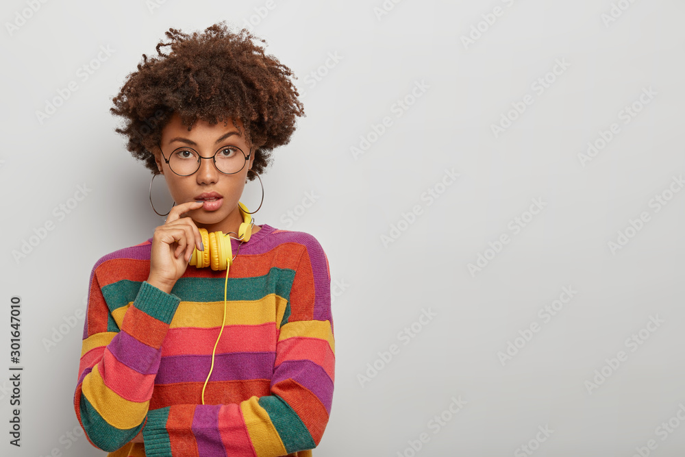 Studio shot of self assured lovely woman with natural curly hair, looks ...