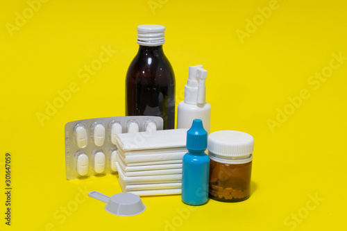 Tissues, nose drops, thermometer, cough syrup, spray, pills and blister on yellow background.