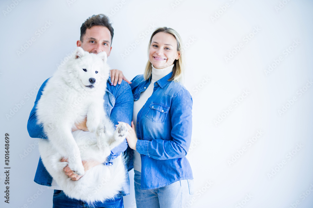 Young beautiful couple holding dog standing over isolated white background Young beautiful couple holding dog standing over isolated white background