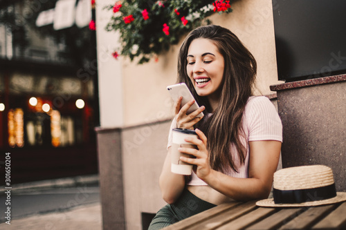 Beautiful woman using phone and drink coffee sitting on street cafe.