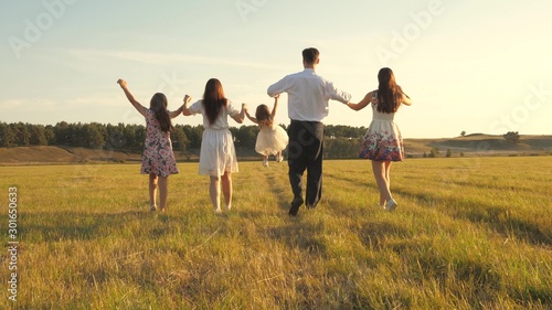 mother  father and little daughter with sisters walking in field in the sun. Happy young family. Children  dad and mom play in meadow in the sunshine. concept of happy family.