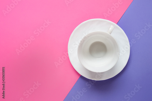 Single one porcelain white empty cup on a dish on pink purple double background. Photo with copy blank space.