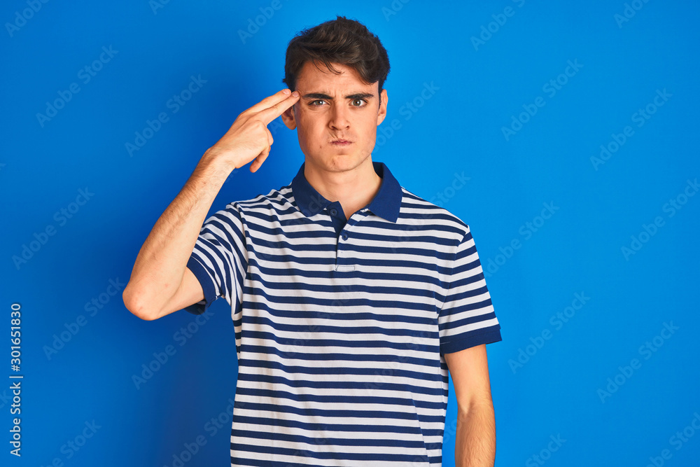 Teenager boy wearing casual t-shirt standing over blue isolated background Shooting and killing oneself pointing hand and fingers to head like gun, suicide gesture. Teenager boy wearing casual t-shirt standing over blue isolated background Shooting and killing oneself pointing hand and fingers to head like gun, suicide gesture.