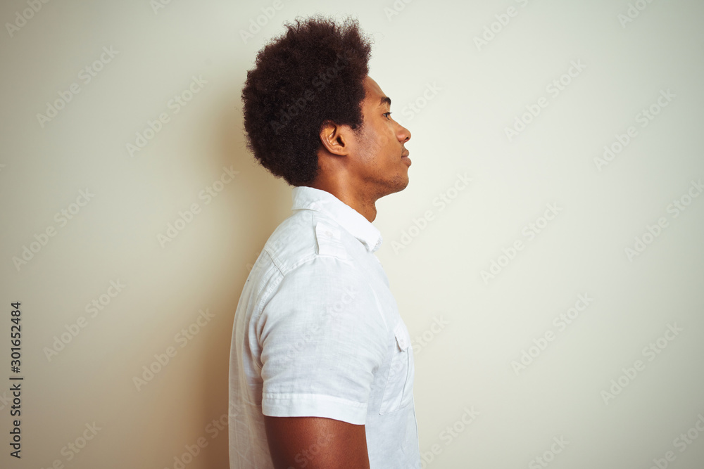 African american man with afro hair wearing shirt standing over isolated white background looking to side, relax profile pose with natural face with confident smile. African american man with afro hair wearing shirt standing over isolated white background looking to side, relax profile pose with natural face with confident smile.