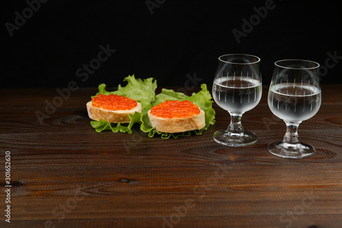 background with sandwiches with red caviar. two glasses of cold vodka
