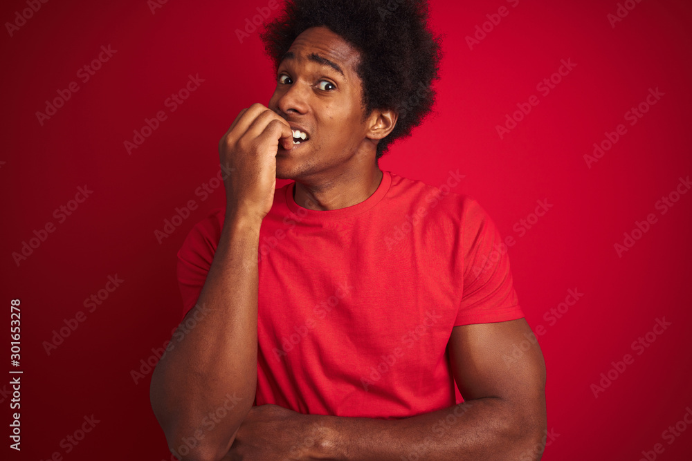 Young american man with afro hair wearing t-shirt standing over isolated red background looking stressed and nervous with hands on mouth biting nails. Anxiety problem.